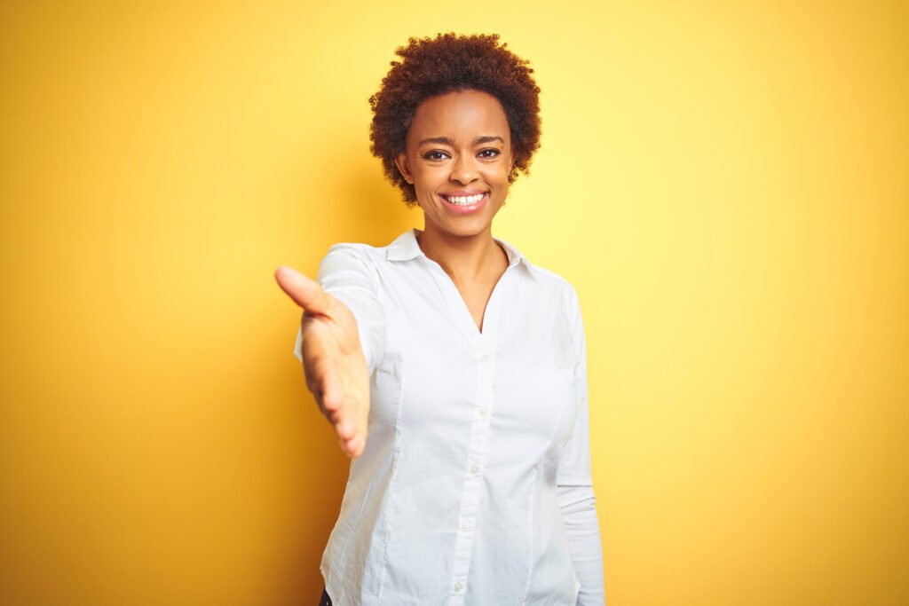 African american business woman over isolated yellow background smiling friendly offering handshake as greeting and welcoming. Successful business. African american business woman over isolated yellow background smiling friendly offering handshake as greeting and welcoming. Successful business.
