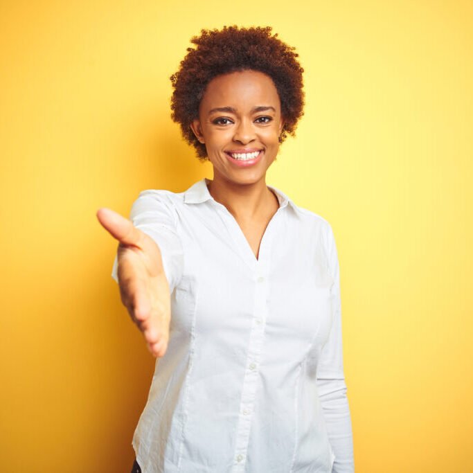 African american business woman over isolated yellow background smiling friendly offering handshake as greeting and welcoming. Successful business. African american business woman over isolated yellow background smiling friendly offering handshake as greeting and welcoming. Successful business.
